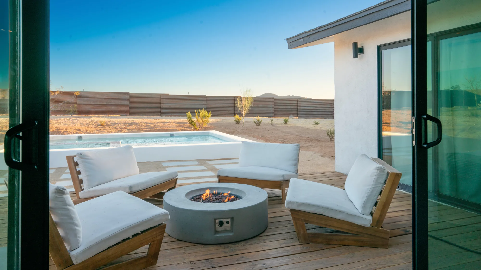 Lit fire pit and teak lounge chairs on the deck beside the pool