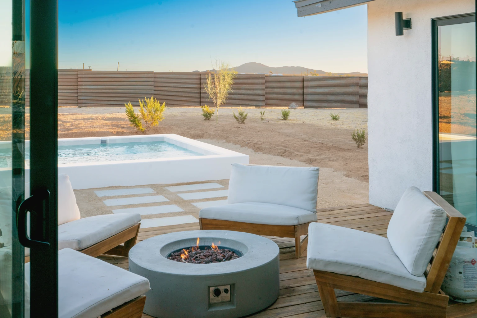 Fire pit lit at golden hour on the deck, lounge chairs and the pool beyond, Joshua Tree California